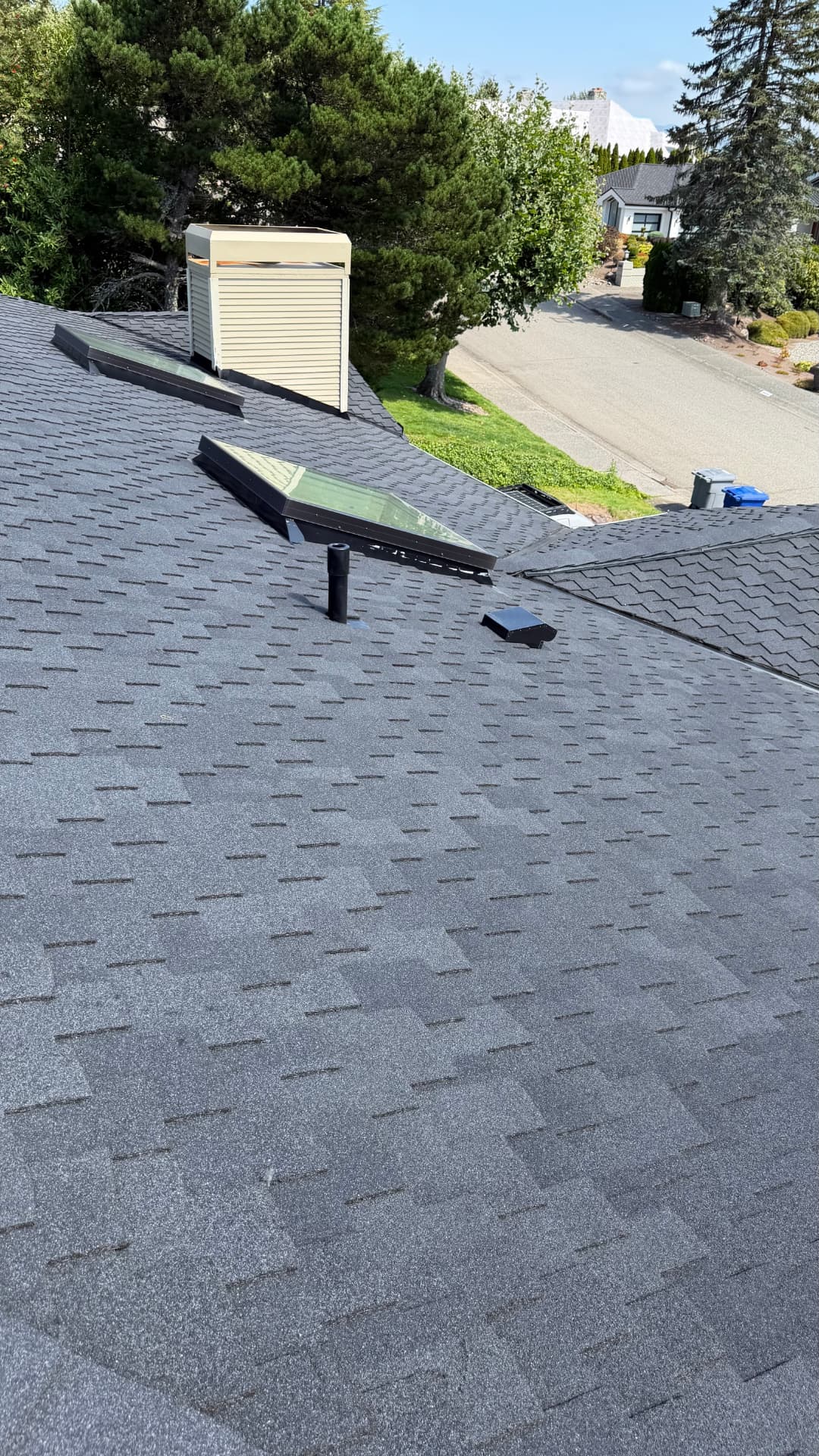 Aerial view of a finished shingle roof with skylights above a quiet neighborhood street